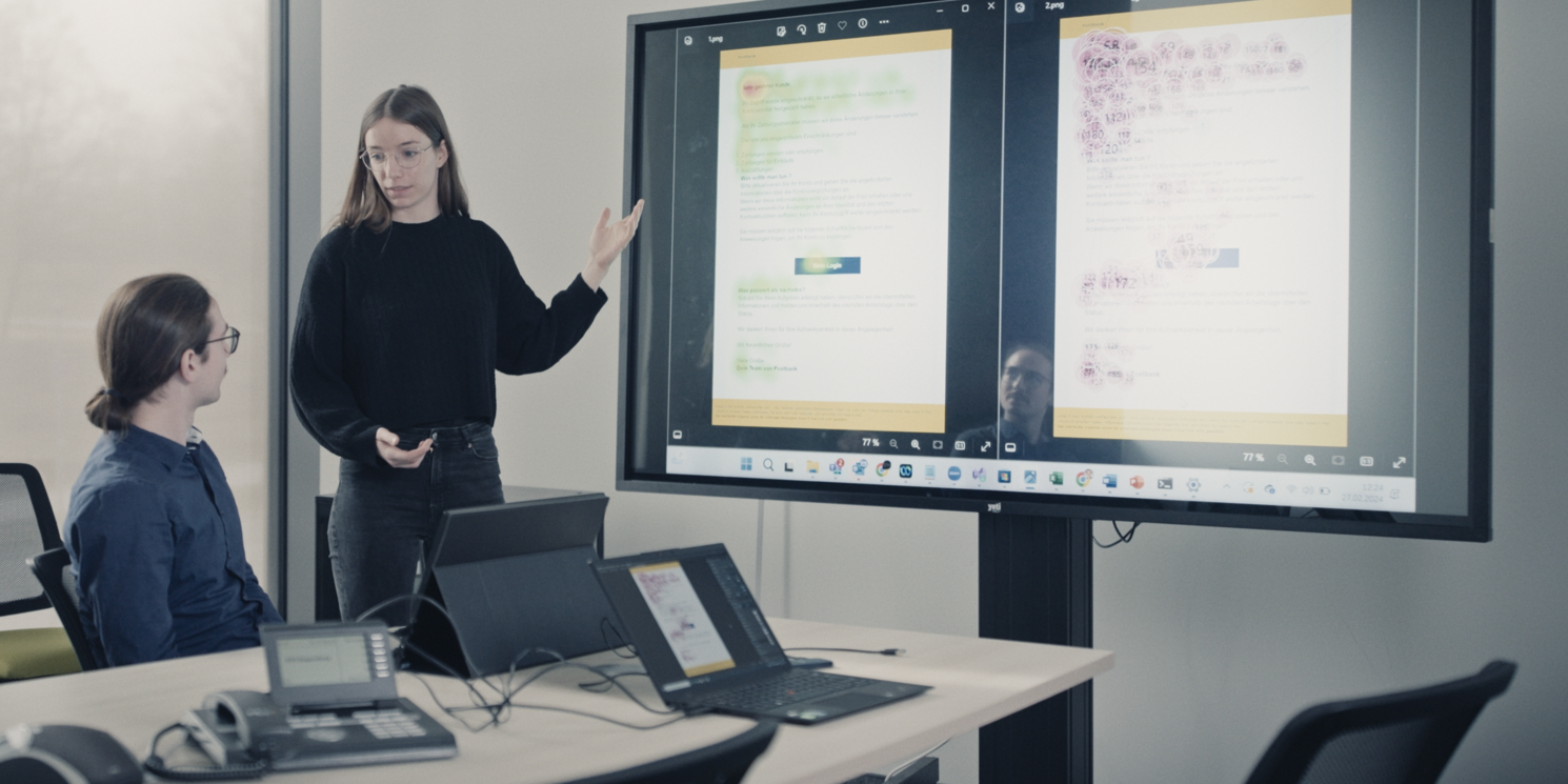 Meret Kristen und Fabian Engl stehen in einem Seminarraum an der OTH Regensburg und werten gemeinsam Daten vor einer großen Leinwand aus. Links und rechts ist eine Heatmap zusehen, die farbige Flecken aufweist und so Informationen übermittelt.