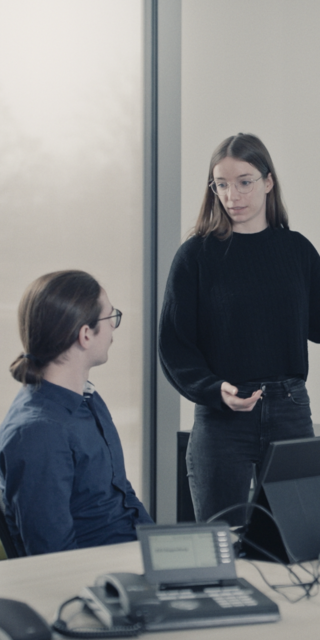 Meret Kristen und Fabian Engl stehen in einem Seminarraum an der OTH Regensburg und werten gemeinsam Daten vor einer großen Leinwand aus. Links und rechts ist eine Heatmap zusehen, die farbige Flecken aufweist und so Informationen übermittelt.