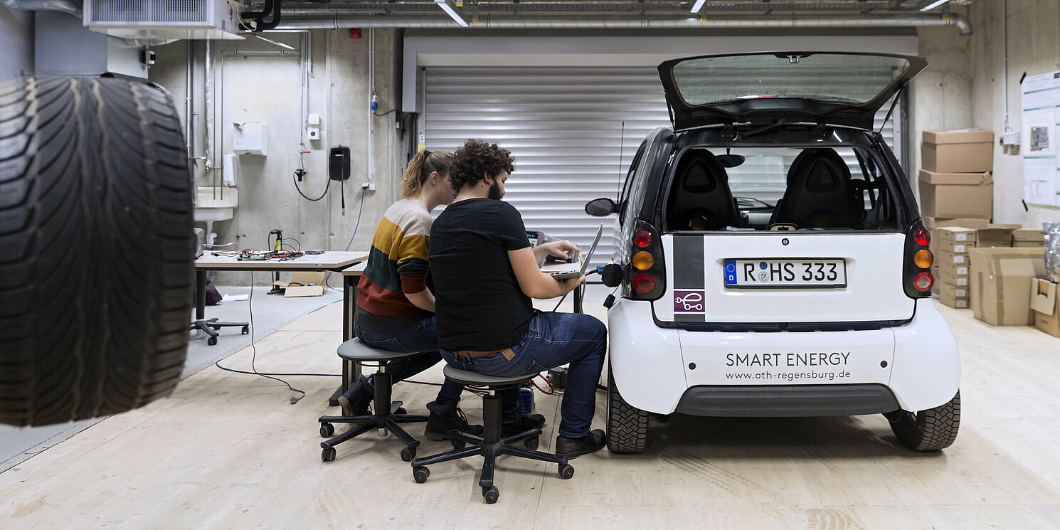 Zwei Studierende führen Messungen an einem E-Auto im Labor durch